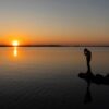 Man holding head sadly while looking at the water at sunset