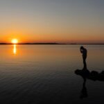 Man holding head sadly while looking at the water at sunset