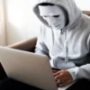 Hacker in a mask and hoodie at a computer