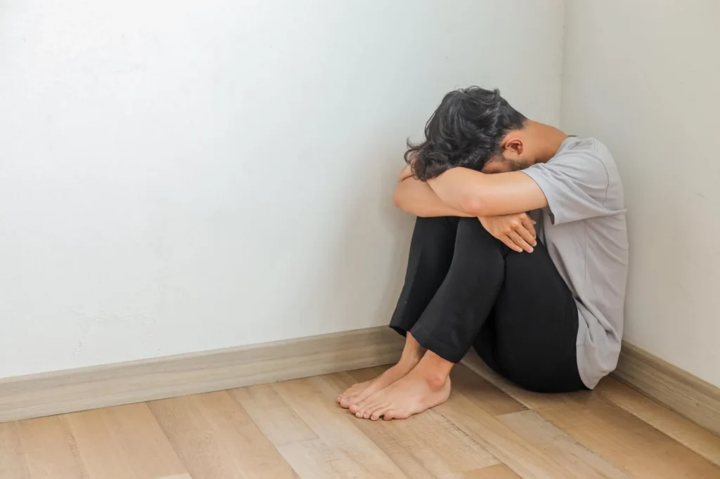 Depressed young man sitting on the floor in the corner of their room