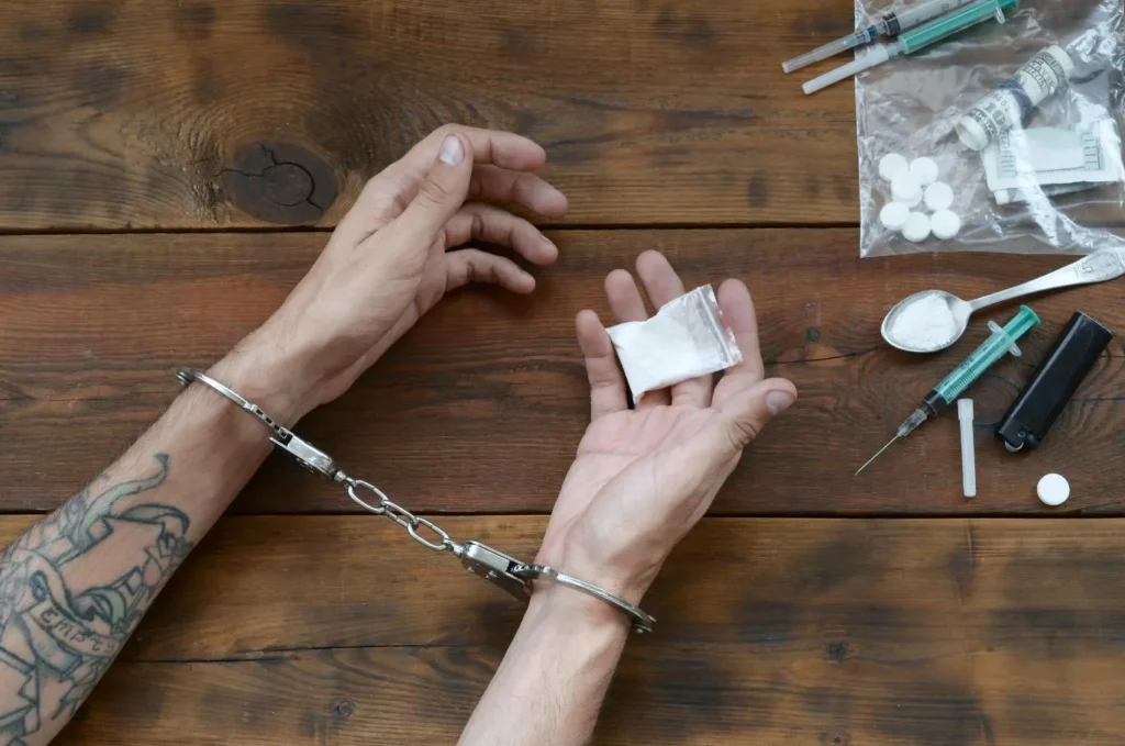 Someone in handcuffs holding a small bag of drugs