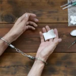 Someone in handcuffs holding a small bag of drugs