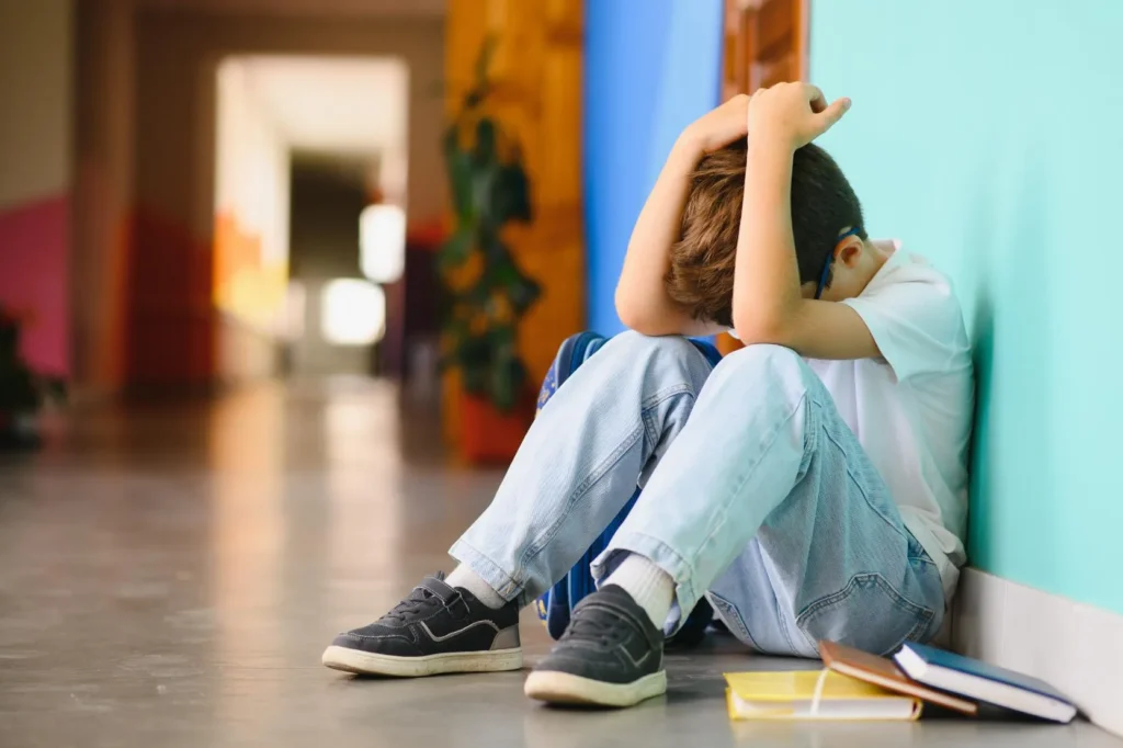 Little boy sitting in the corner with his head in his hands