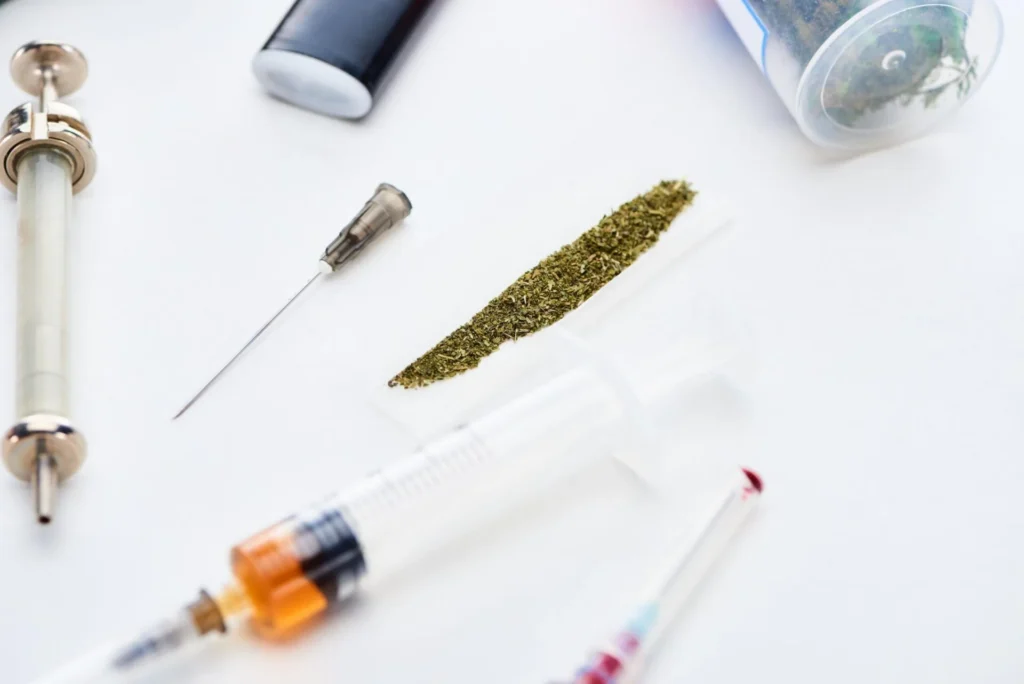 Several substances on a table: weed, syringes, lighters, and more